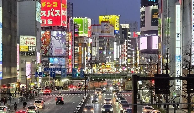 夜晚的东京街区灯光明亮,车流与行人穿梭其间,部分店家看板依旧亮起