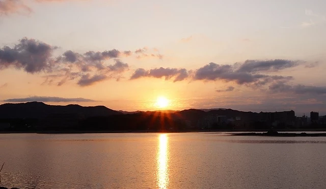 太阳于元旦清晨从山脉后方升起,金色阳光映照在平静的水面上