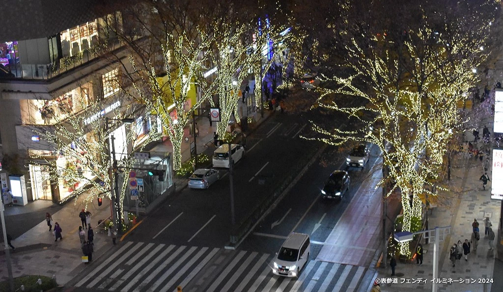 俯瞰东京表参道夜景,街道两侧的榉树点缀满香槟金色灯光,行人与车辆穿梭其中,呈现华丽冬季景象