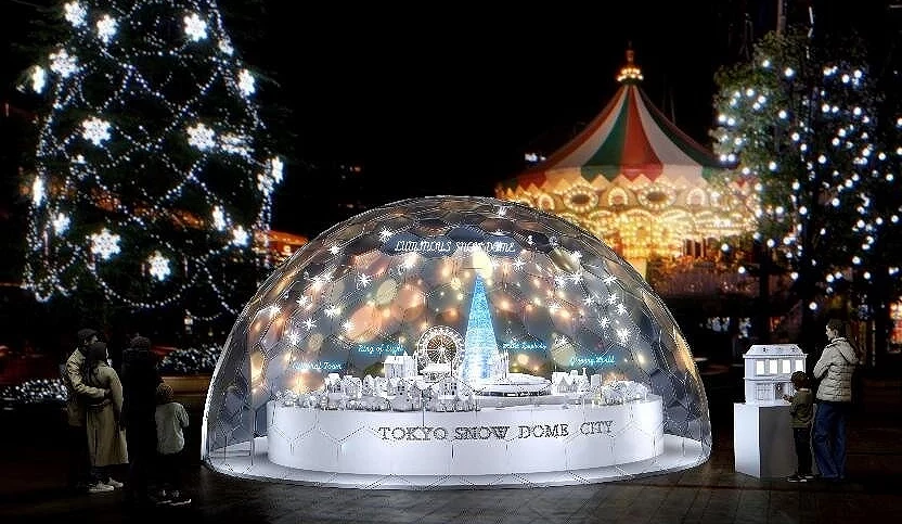 夜晚的东京巨蛋城展示巨型透明雪球造景,内部有迷你城市模型与蓝色圣诞树发光,背景可见旋转木马与灯光装饰,气氛浪漫温馨