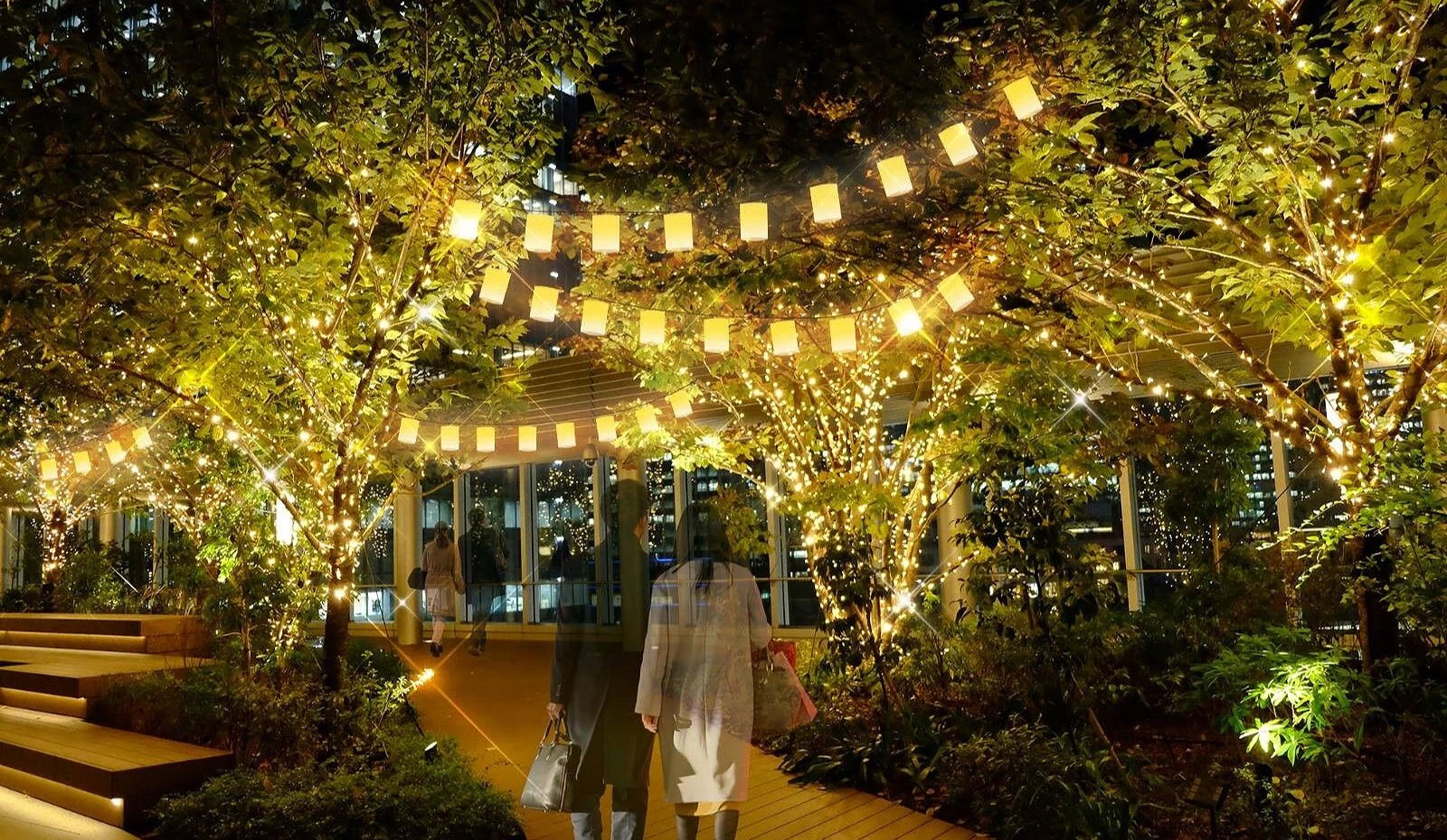 东京中城八重洲露台夜景,树木与吊灯被香槟金灯饰点亮,游客漫步其中气氛浪漫