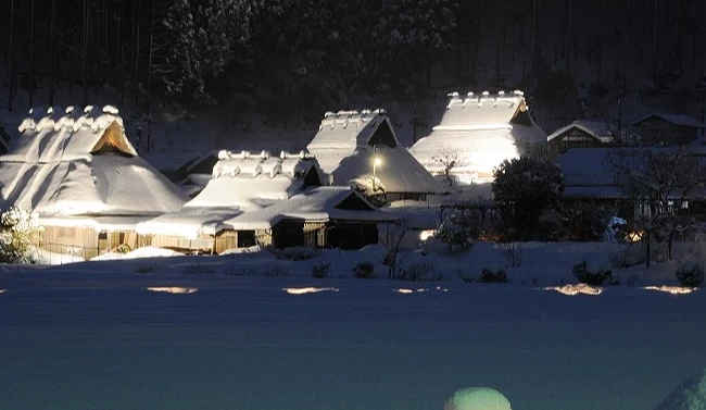 夜晚被雪覆盖的茅葺屋,周围点亮着灯