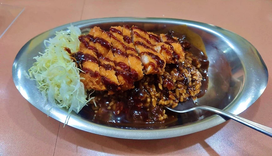 搭配高麗菜絲、炸物和金屬盤的深色金澤咖哩