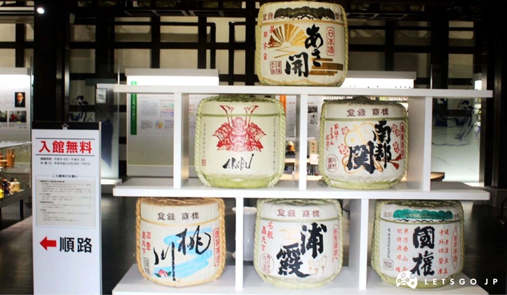 南部杜氏傳承館內,展示著六個不同清酒品牌的酒樽,酒樽以稻草繩捆綁,放置於白色架子上。左側可見「入館無料」與「順路」指示牌。