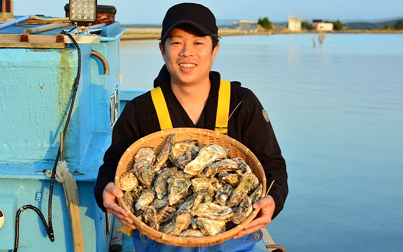戴黑色帽子的男生站在船中,手拿一籃牡蠣
