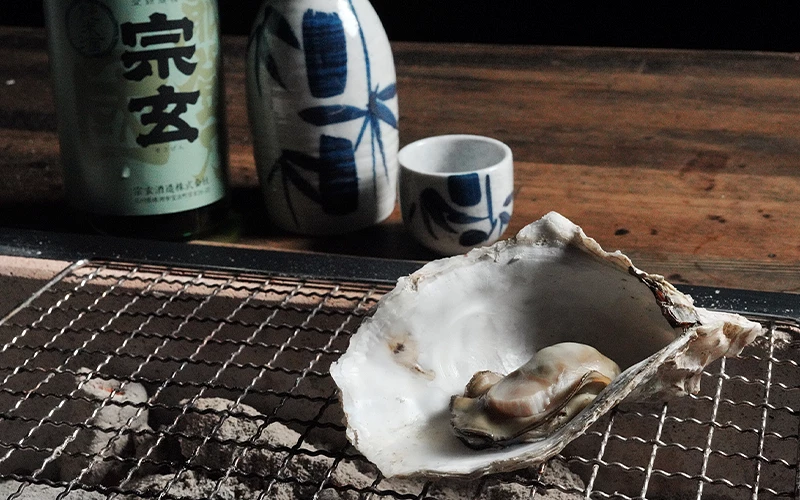 烤網上的帶殼牡蠣前放有標示「宗玄」字樣的清酒瓶與酒杯