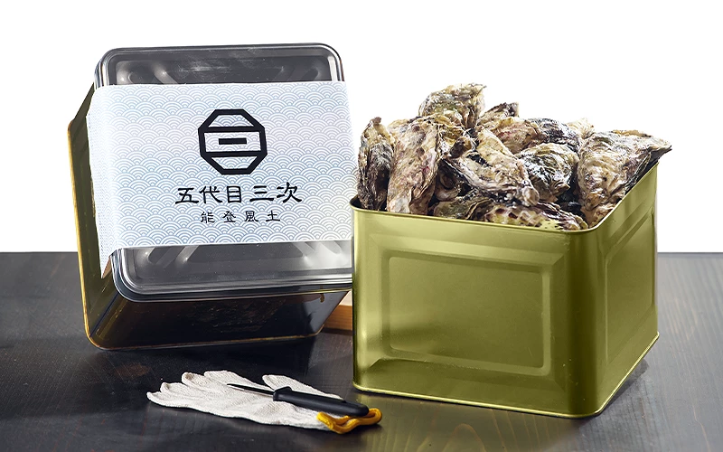 金屬盒裝滿帶殼牡蠣,旁放印有「五代目三次 能登風土」字樣的外盒