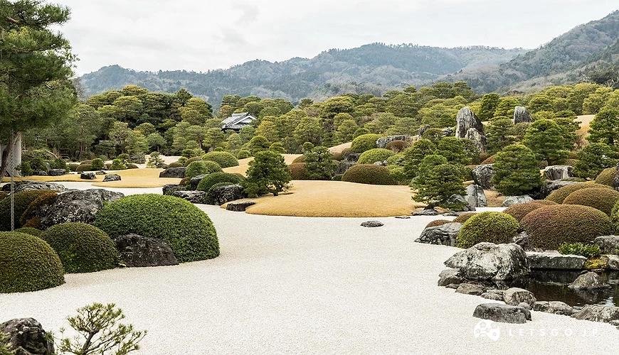 足立美術館日式庭園全景,白砂庭與修剪灌木、巨石配置,遠方山景作背景