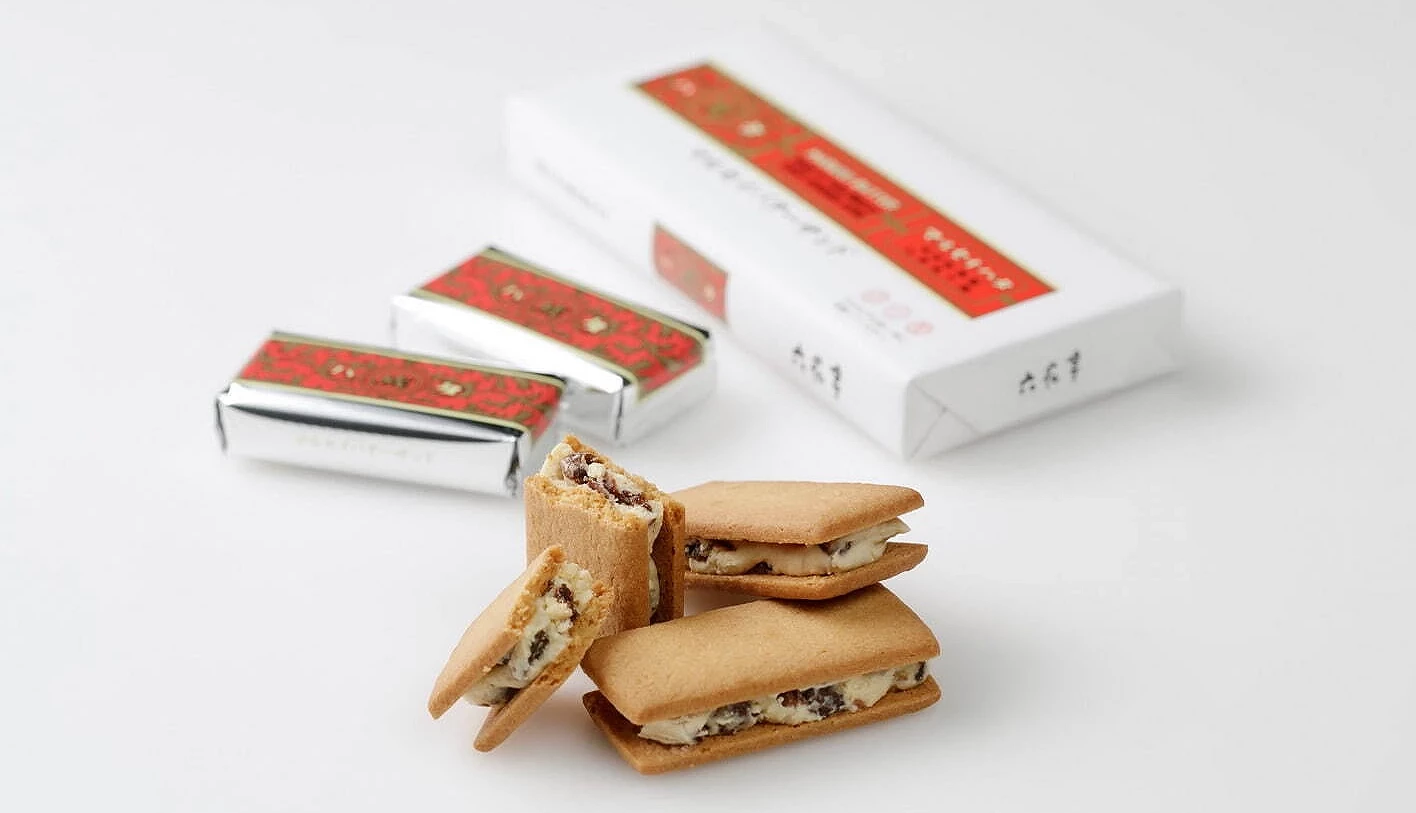 桌面上摆放数块六花亭奶油葡萄夹心饼,切面可见奶油与葡萄干内馅;背景有银色独立包装与白色长方形外盒