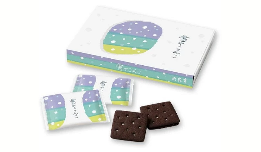 六花亭「雪やこんこ」饼干的包装与实物示意,外盒与独立包装以紫、绿、蓝的雪景插画设计,前方展示两片深色可可饼干,可见其薄脆质地与白色夹心的孔洞造型