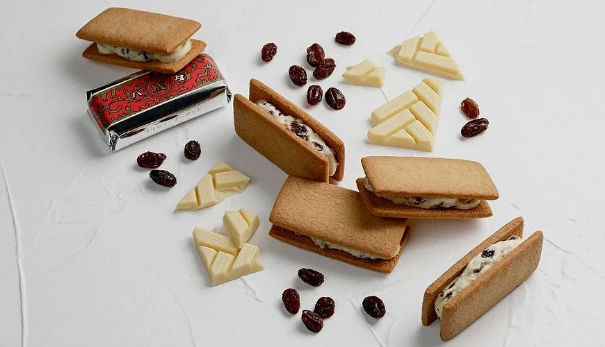 六花亭兰姆葡萄奶油夹心饼干,香脆饼干夹入奶油与兰姆葡萄干,搭配白巧克力碎与葡萄干平铺于背景