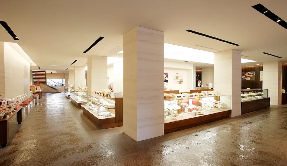 带广六花亭本店店内宽敞明亮的贩售区,整排玻璃甜点柜整齐陈列蛋糕与点心,采用浅色系石材与木质装潢