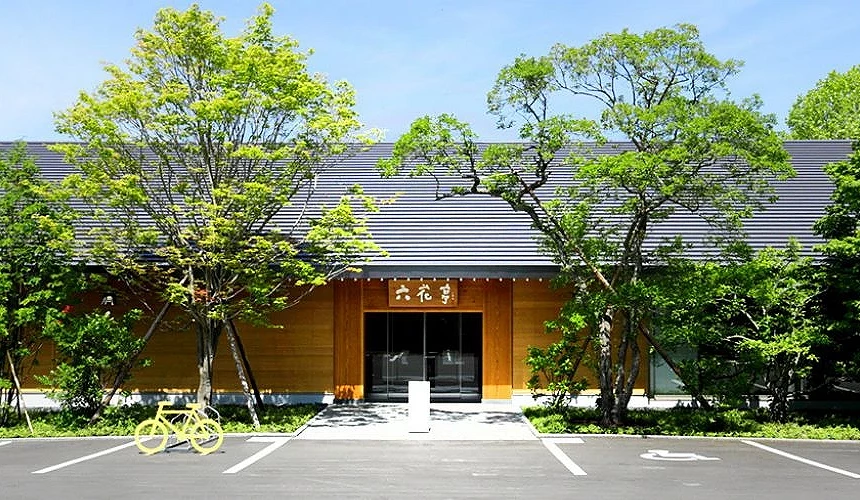 六花亭旭川神乐冈店的外观,木质墙面搭配深色屋顶,周围环绕茂盛绿树,门前设有停车空间