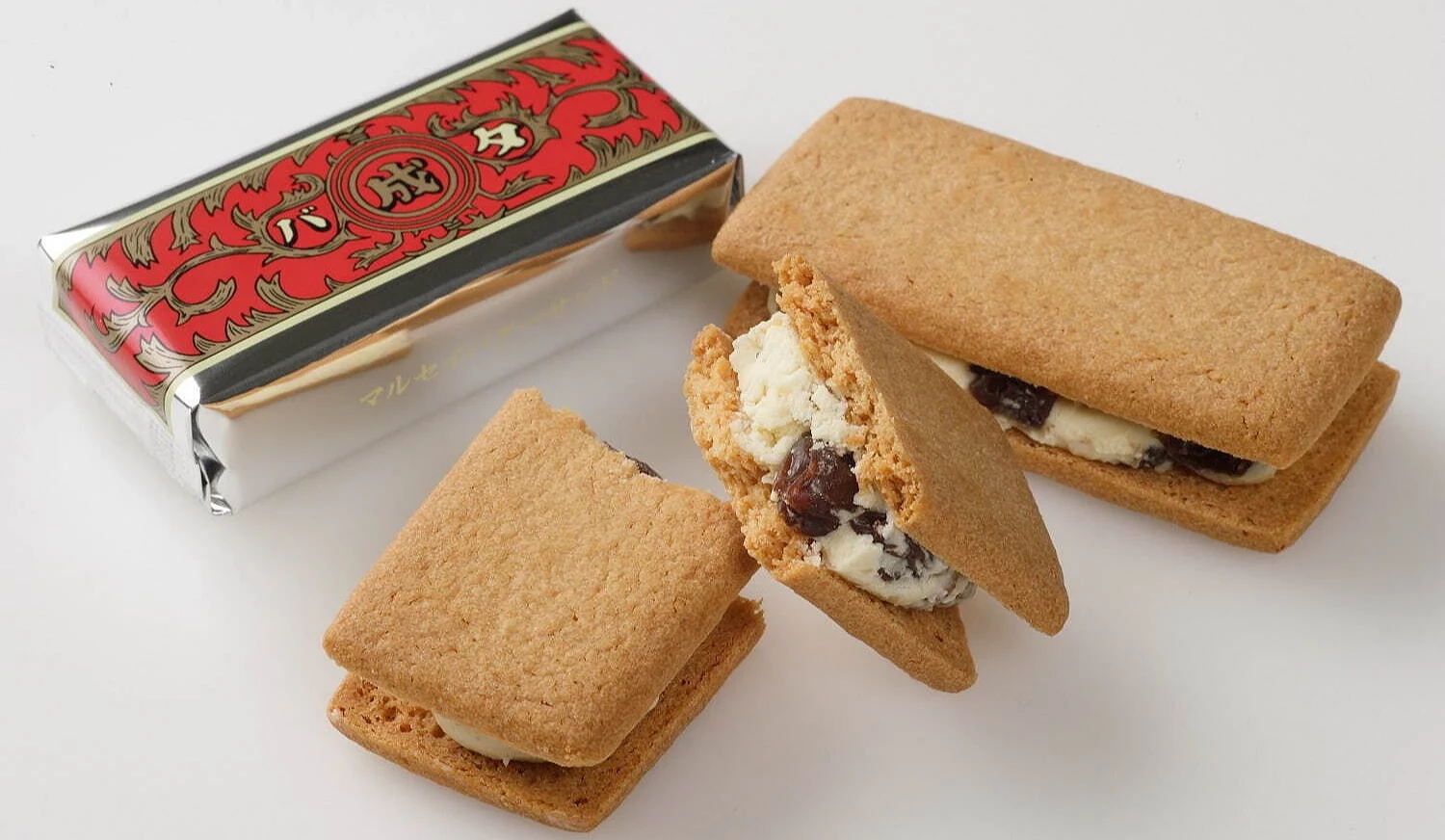 六花亭マルセイ奶油葡萄夹心饼,以酥脆饼干夹入奶油与兰姆葡萄干,前景为切开的夹心饼,后方可见红金包装的个别外袋