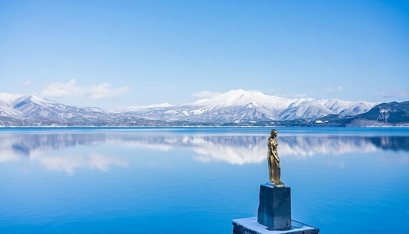 湖上倒映雪山与金色雕像