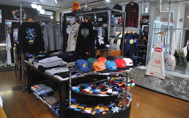 室內服飾陳列架擺放帽子、上衣與外套,中央圓桌展示多色襪子與帽款