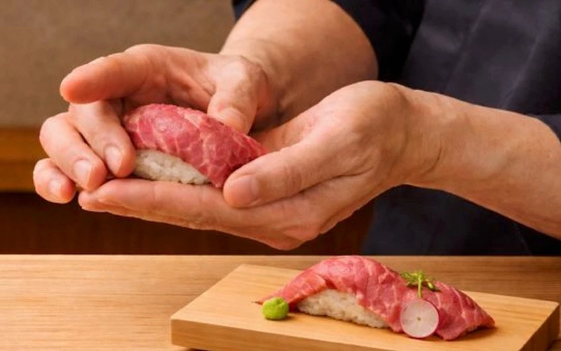 廚師雙手捏製牛肉壽司，壽司放在木板上