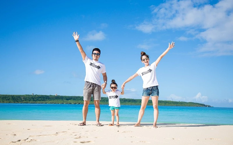 沙灘上一家三口牽手站立，三人穿著印有 BEACH 字樣白色上衣