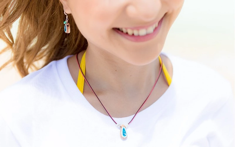女子微笑特寫，配戴藍色水滴造型項鍊與耳環