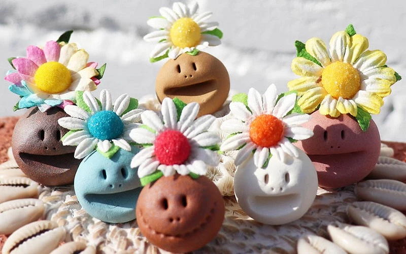 多個彩色陶製小人偶，頭戴花朵裝飾擺放在貝殼上