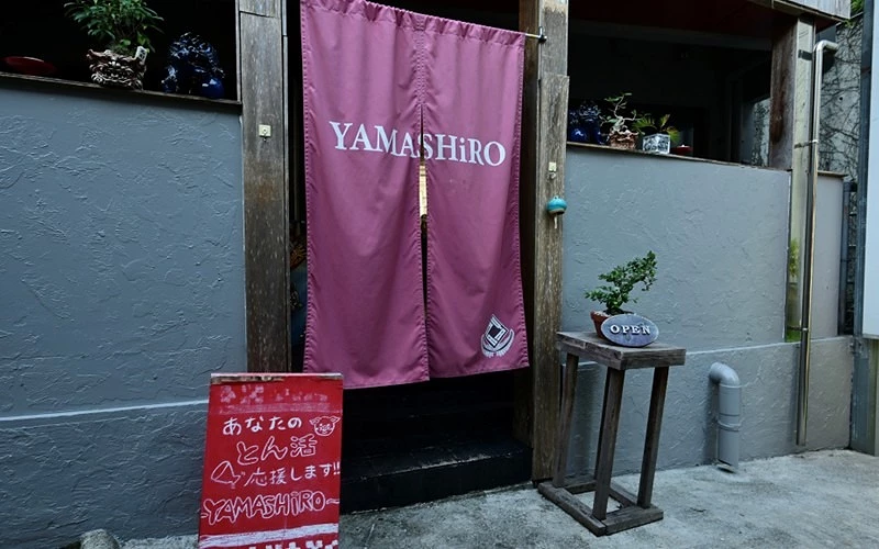 位於沖繩的餐廳YAMASHiRO門口外觀有著紅色長版暖簾上印著英文YAMASHiRO