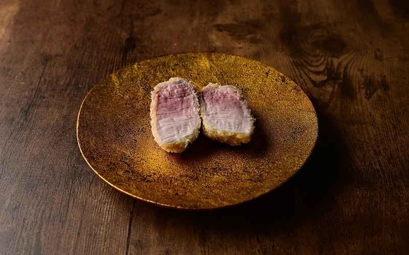 粉紅白相間的炸肉剖面排擺放在金色圓盤上