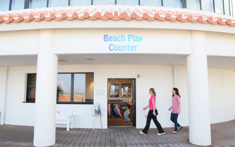 兩個人經過一棟白色建築物上方有英文字beachplaycounter