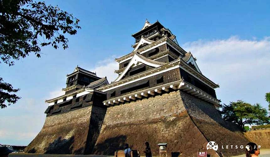 熊本城黑色多层天守阁耸立于大型石垣之上,底部可见游客身影