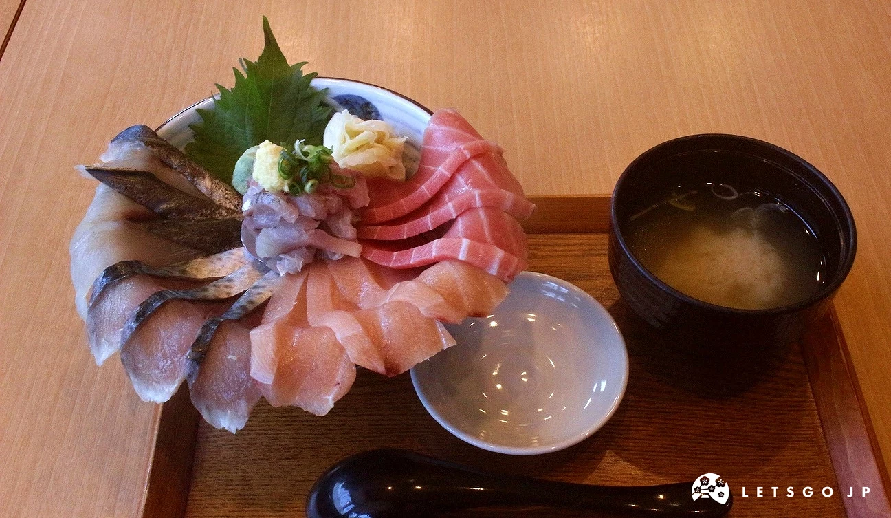 木托盤上盛裝一碗華麗的海鮮丼飯，上鋪滿鮪魚、鯖魚等多種厚切生魚片，附上一碗味噌湯。