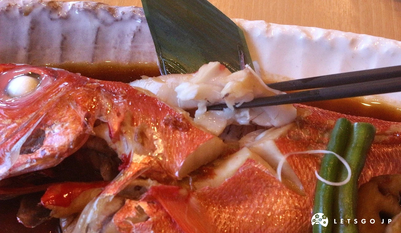 用筷子夾起紅燒金目鯛白嫩魚肉的近照，旁邊有鮮綠色的配菜。