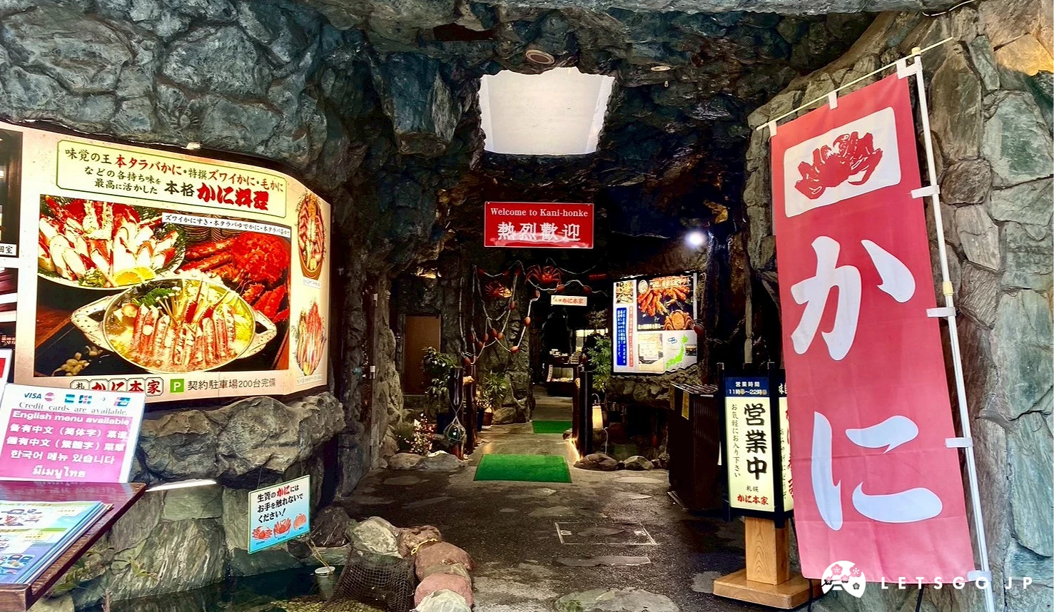 札幌螃蟹本家仙台店的入口實景，石牆結構搭配日式紅色布簾與菜單告示牌，呈現獨特的洞窟風格走廊。