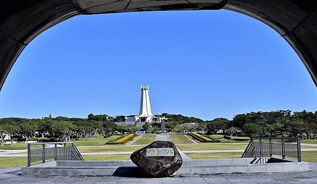 冲绳和平祈念公园景象,广阔草地与纪念碑轴线延伸,中央白色和平纪念塔矗立于蓝天下