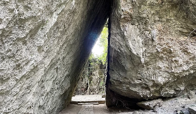 斋场御岳三库理景象,两块巨大岩石形成三角形通道,中央透出光线与远方绿意景色