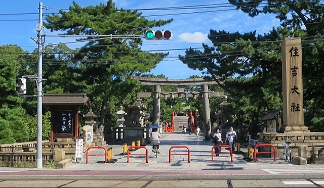 大阪住吉大社正面參道入口,前方可見鳥居與石燈籠,遠方為太鼓橋,畫面包含路面電車軌道與行人