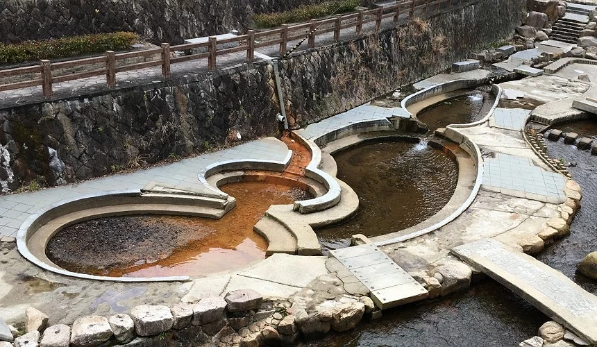有馬溫泉親水公園內的戶外足湯景觀,池水呈現明顯的紅褐色金之湯與透明銀之湯色澤對比。