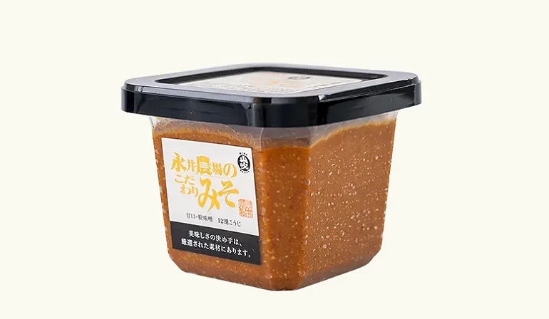 永井农场特制味噌(永井农场のこだわりみそ)的方形透明盒装外观,内容物为深棕色的信州味噌,搭配黑色盖子与白底金黄色字体的标签