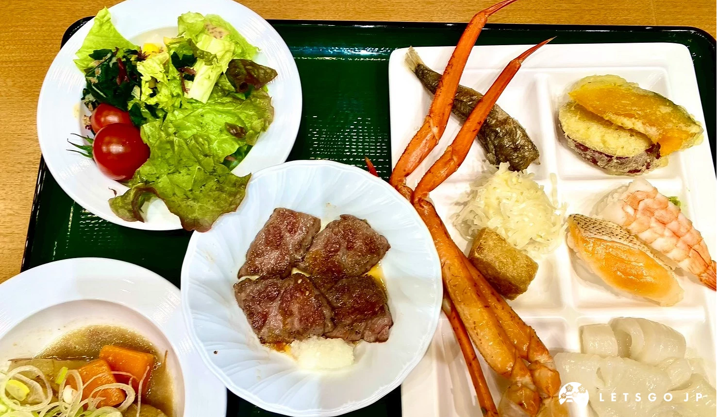 餐盤中裝有松葉蟹腳、生菜沙拉、握壽司與烤牛肉的豐盛晚餐。
