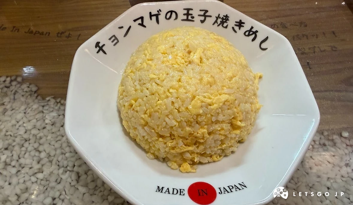 一個白色八角瓷盤,中央盛裝著圓頂形狀的金黃色雞蛋炒飯。盤緣印有「MADE IN JAPAN」黑色小字與「チョンマゲ」日文字樣。