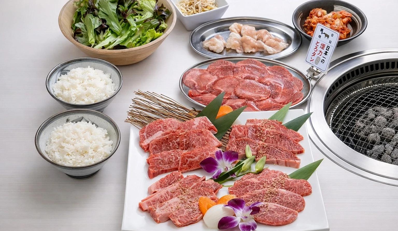 多種燒肉部位、兩碗白飯、湯品、泡菜及沾醬。