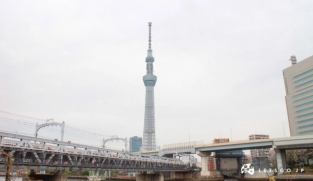 從隅田川岸邊遠眺東京晴空塔,前方為鐵路橋樑。