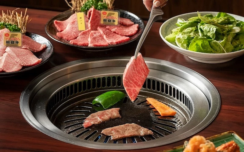 夾起雪花牛肉放上燒肉烤爐旁有蔬菜與沙拉