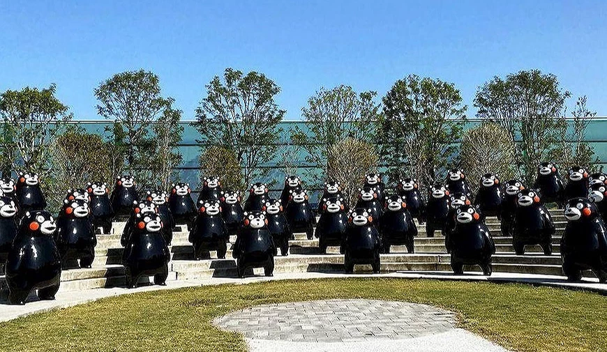 階梯上排列的多個熊本熊雕像,背景為樹木與建築物