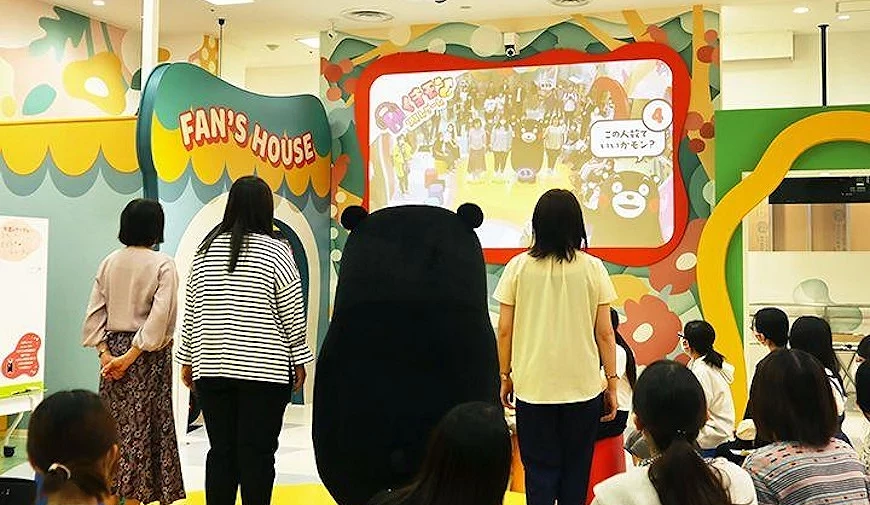 熊本熊與遊客背對鏡頭,觀看標示「FAN'S HOUSE」的互動螢幕