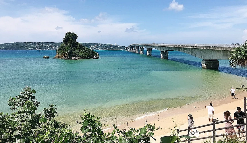 遊客漫步白沙灘,翠藍海水清澈見底,石島與長橋跨越海灣壯觀。