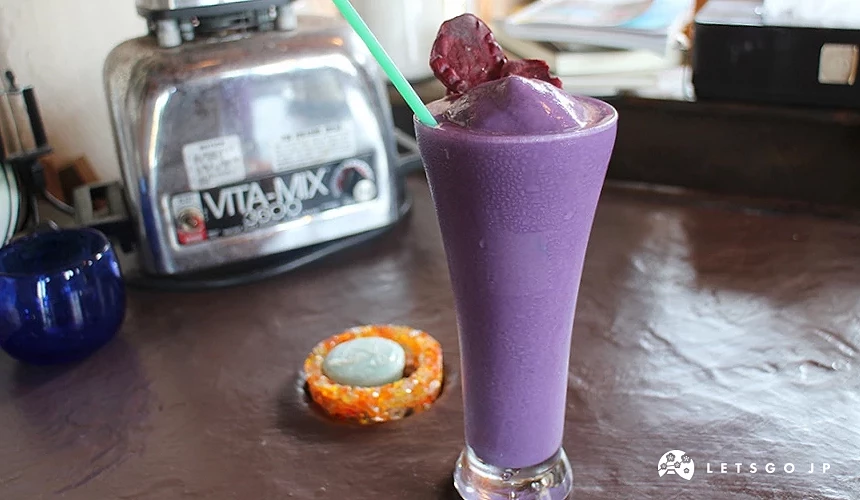 紫色果昔飲品插綠吸管,新鮮水果裝飾杯口,Vitamix調理機與甜點擺放檯面。