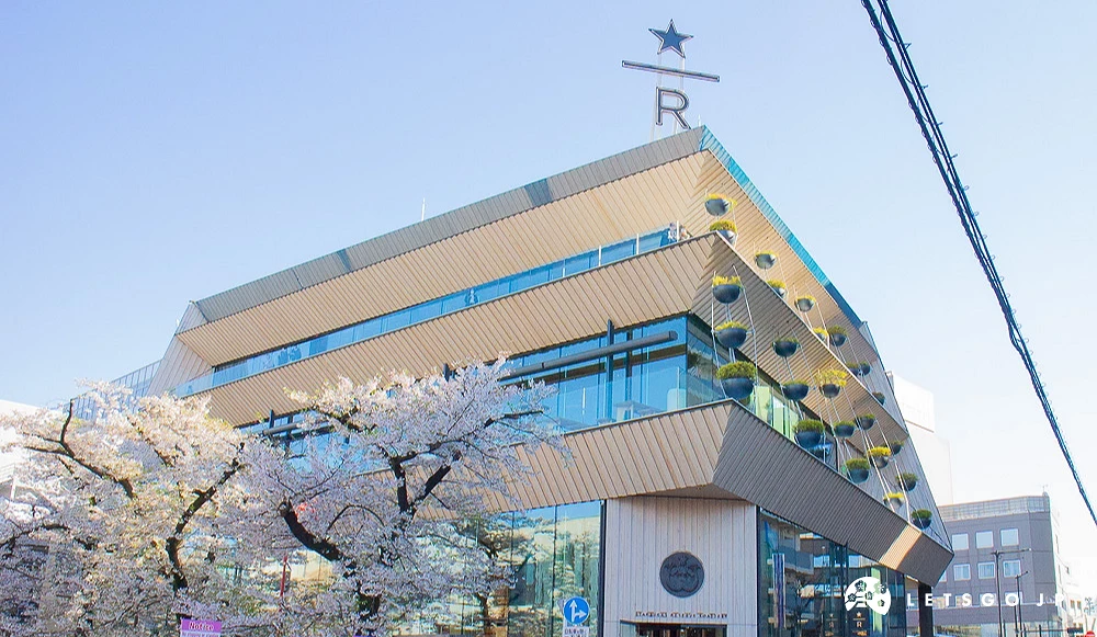 星巴克臻選東京烘焙工坊建築外觀,前方有盛開的櫻花樹與遊客。