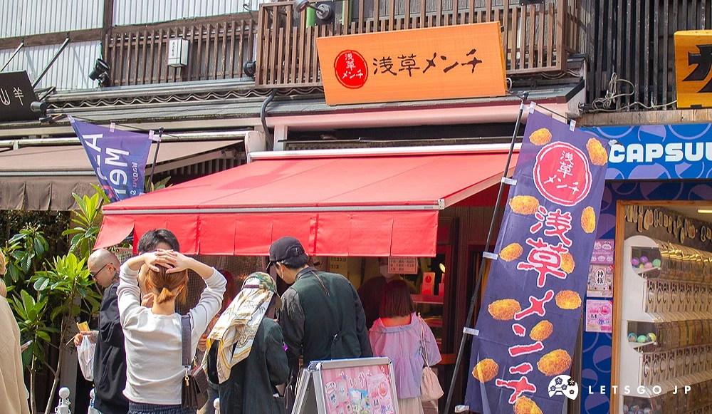 淺草メンチ商店外觀,紅色遮雨棚前有排隊人潮。
