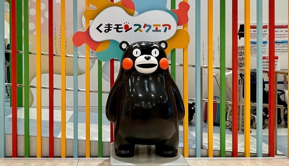 熊本熊立體公仔立於「くまモンスクエア」招牌前彩色條紋背景前