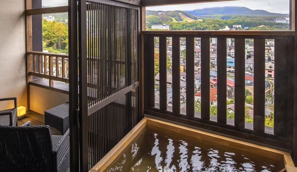 木质方型温泉浴池,水流正注入池中,旁边为设有户外座椅的阳台空间