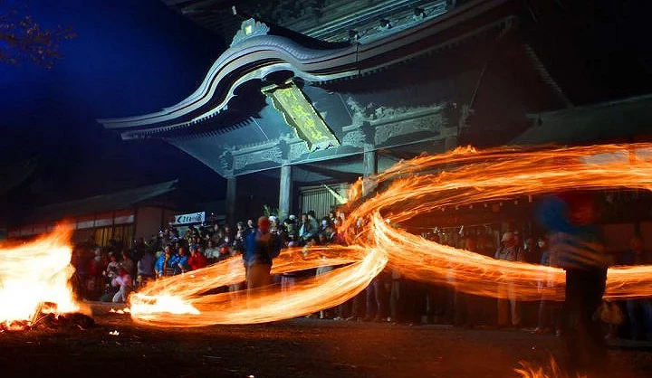 夜晚的阿蘇神社火振神事，參拜者在樓門前揮動燃燒火束，周圍聚集眾多觀眾